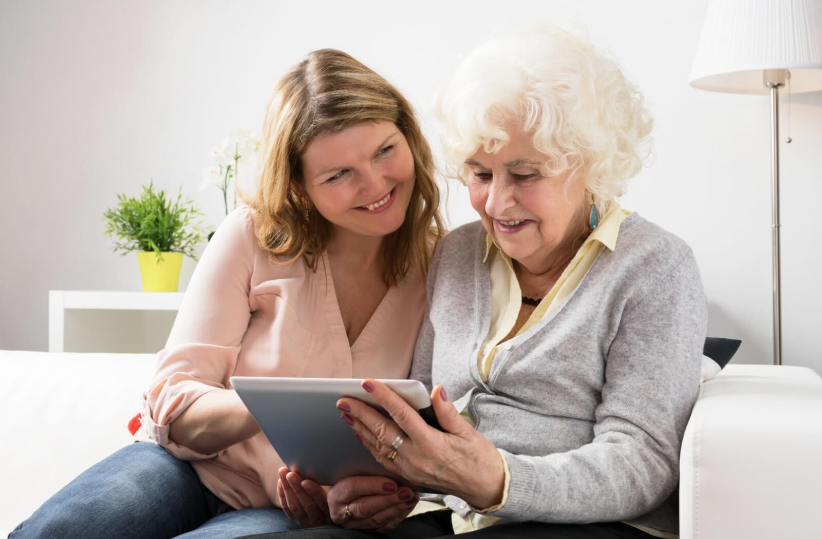 Two people sitting on a couch smiling while using a tablet together during a casual tech activity