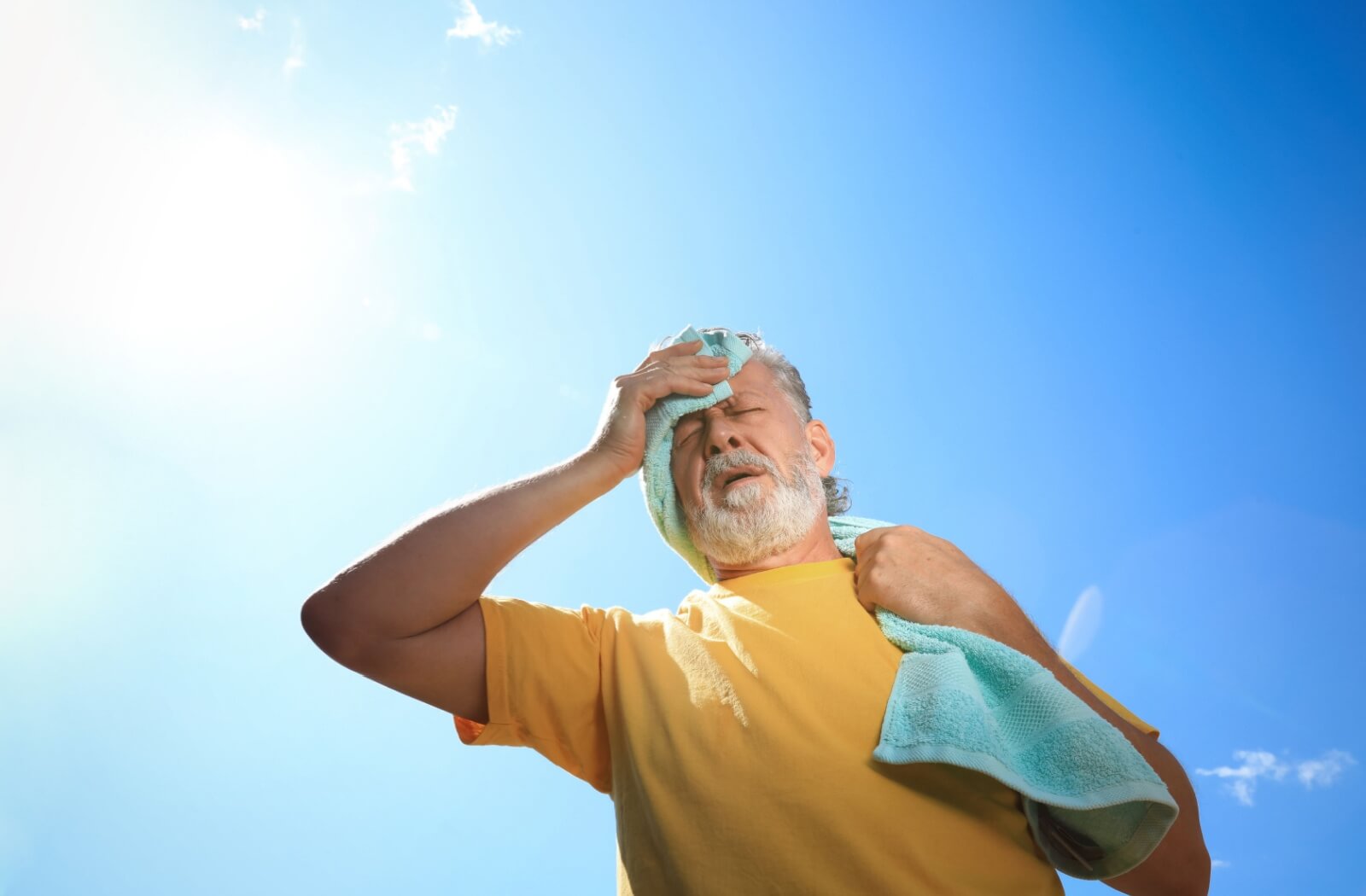 Older adult overheated outdoors using towel for relief under direct sun showing signs of heat stroke and high temperature