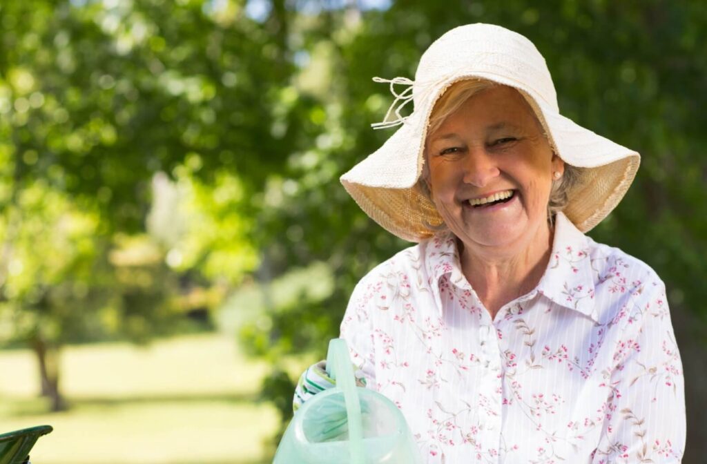 Senior outdoors wearing sunhat smiling while gardening in shade demonstrating safe summer habits for older adults