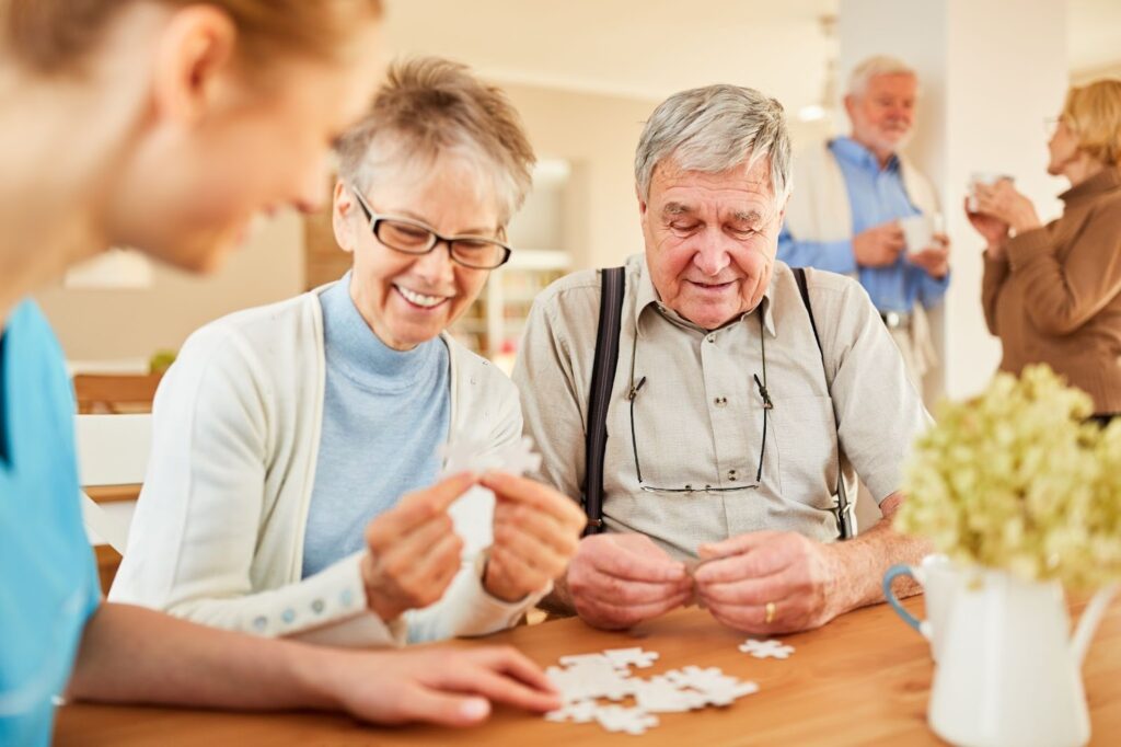 A group of smiling seniors in a memory care community work together on a puzzle.