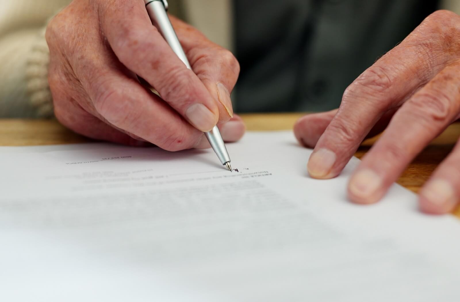 A close-up image of an older adult signing a legal document